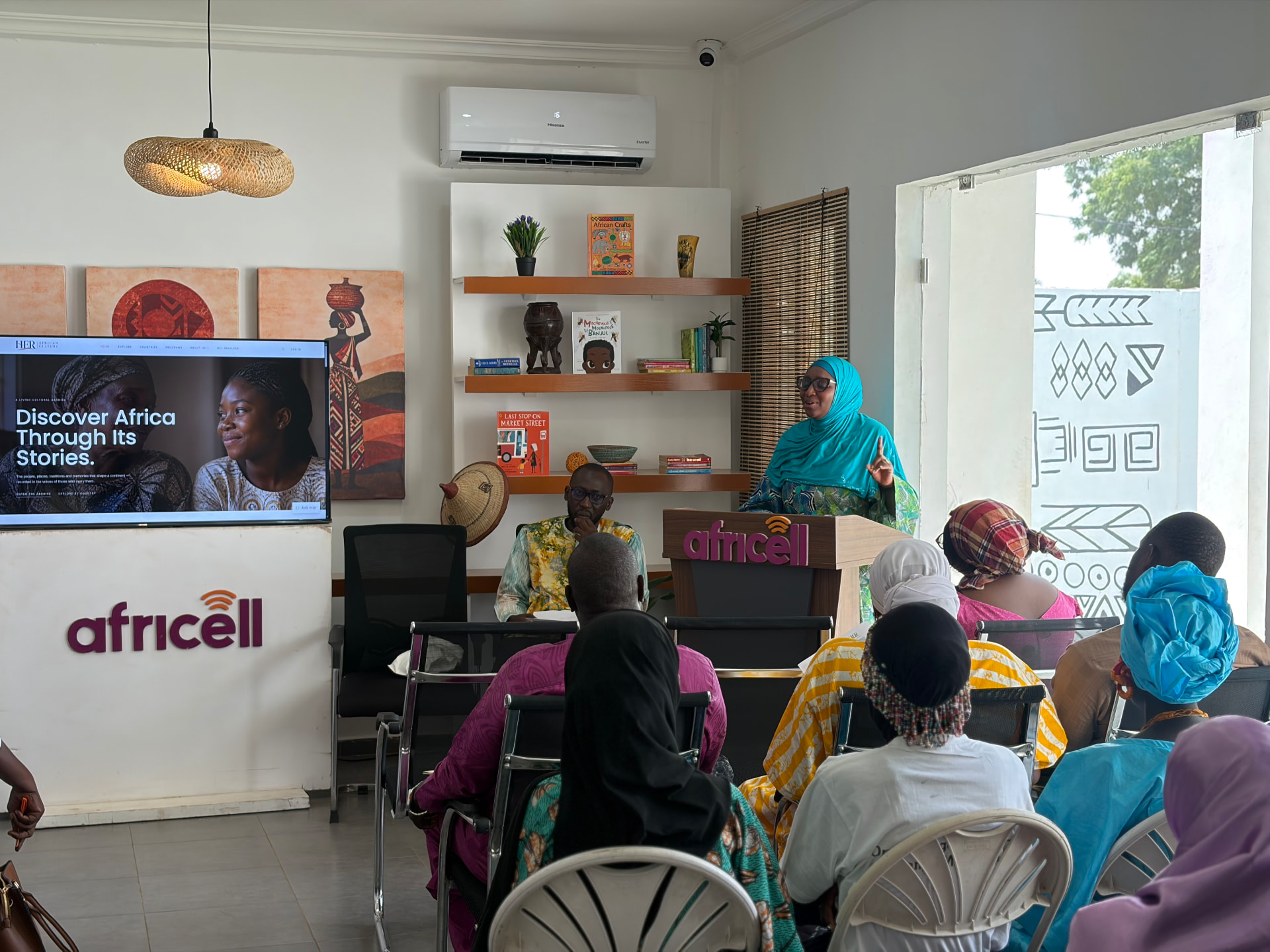 A speaker addressing HERitage Connect attendees at the Africell venue, with Her African Culture displayed on screen